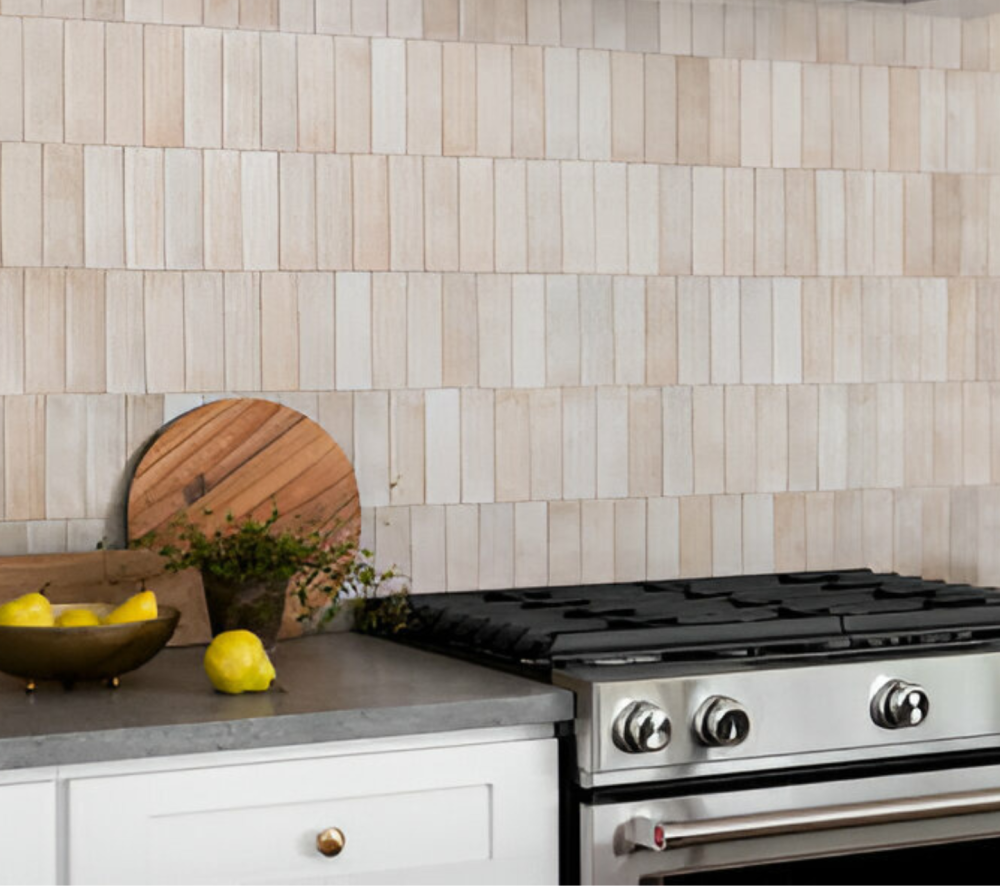 White elongated subway tiles backsplash in a kitchen with a concrete countertop, stainless steel gas range, and white cabinets.