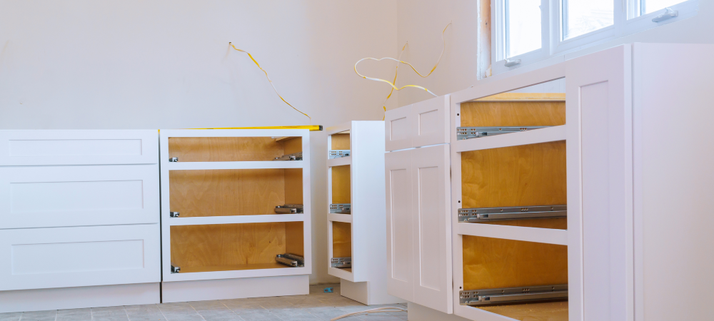 A kitchen renovation in progress, showcasing the installation of white kitchen base cabinets with drawers and shelves.