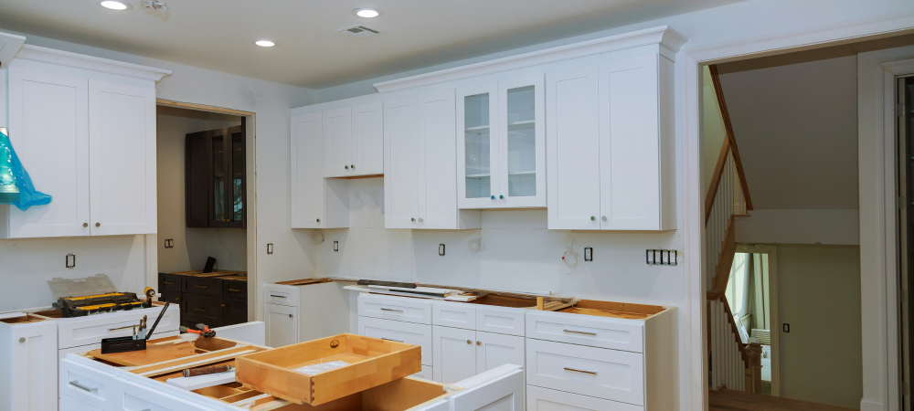 A kitchen with white cabinets being installed, with plastic covering the cabinets to protect them from damage during the renovation process.