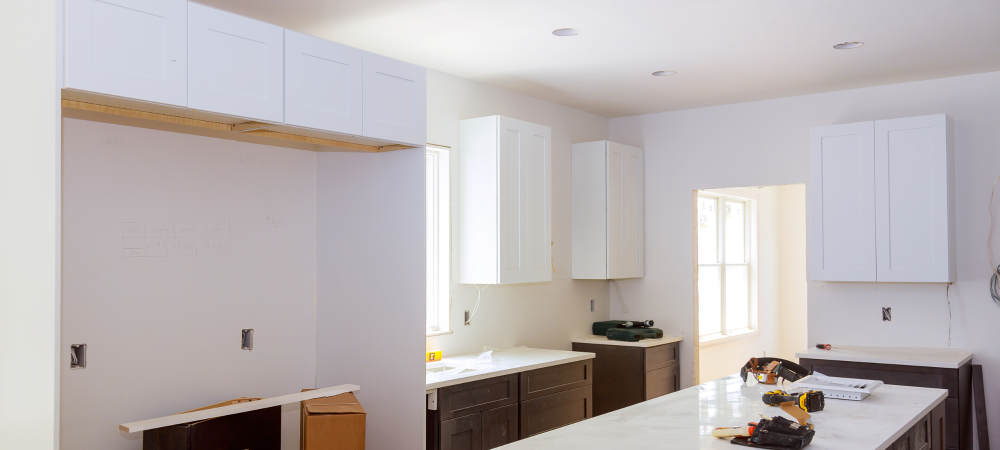 A kitchen under construction with white cabinets installed, showcasing a ledger board used to support the upper cabinets.