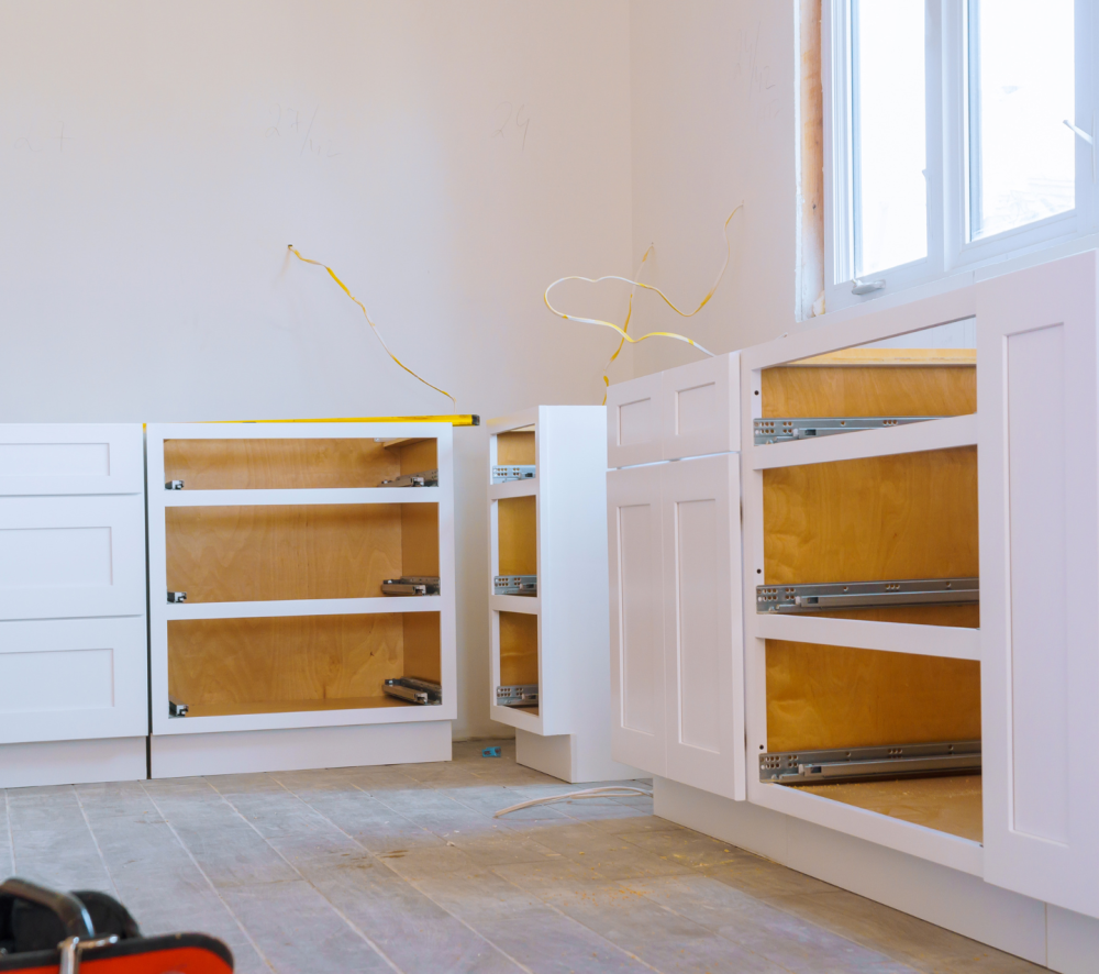 A kitchen renovation in progress, showcasing the installation of white kitchen base cabinets with drawers and shelves.