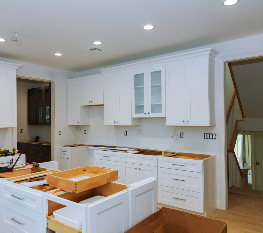 A kitchen with white cabinets being installed, with plastic covering the cabinets to protect them from damage during the renovation process.