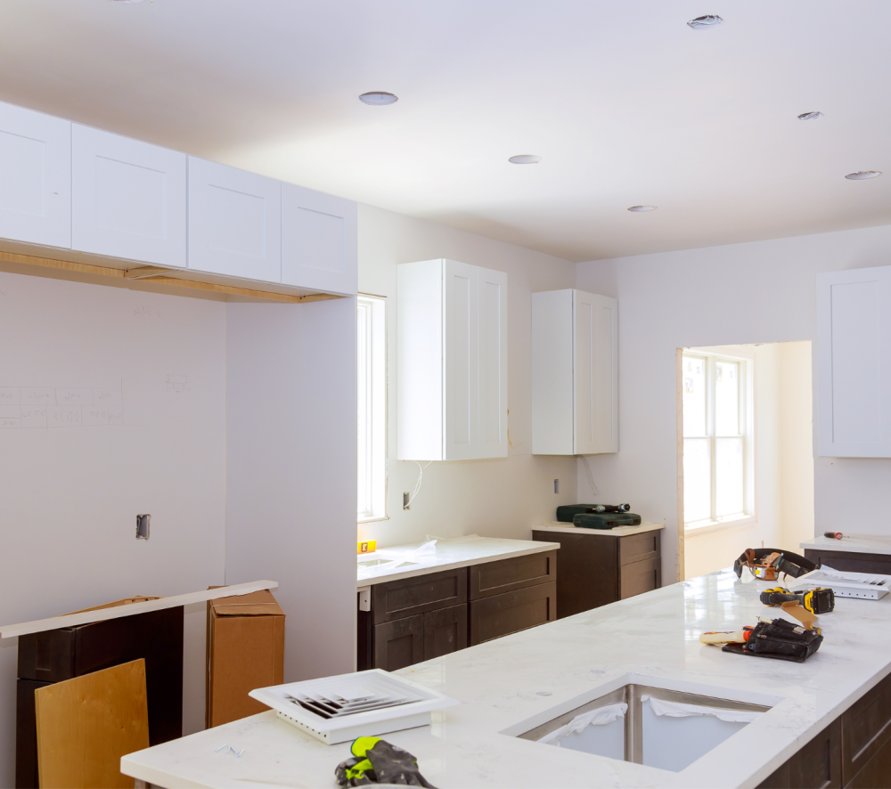 A kitchen under construction with white cabinets installed, showcasing a ledger board used to support the upper cabinets.