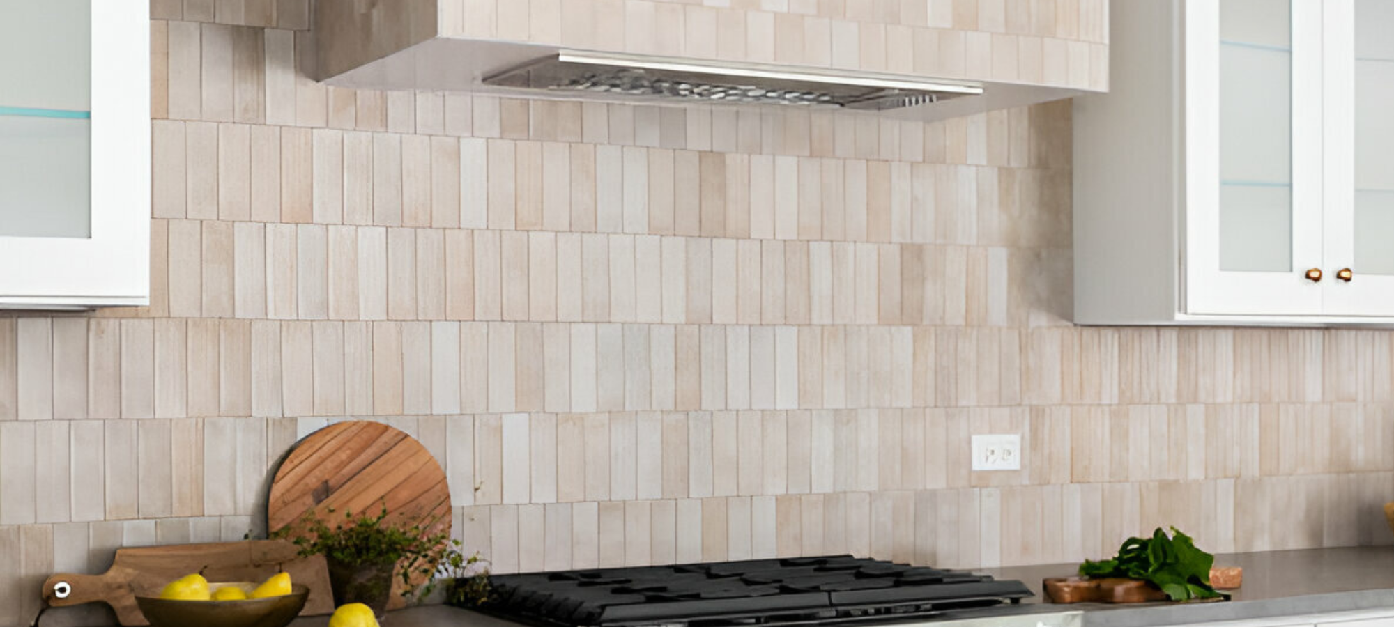 White elongated subway tiles backsplash in a kitchen with a concrete countertop, stainless steel gas range, and white cabinets.